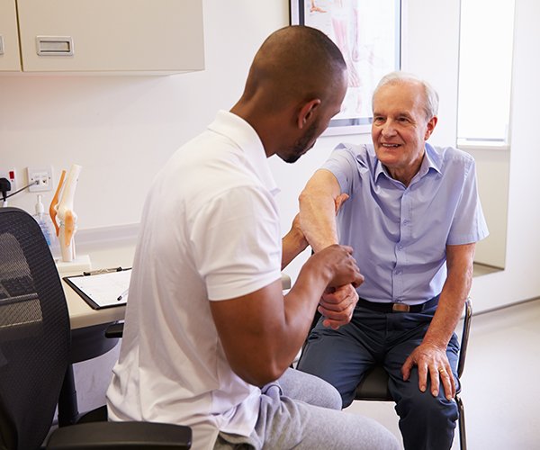 Physiotherapist helping older man with shoulder pain